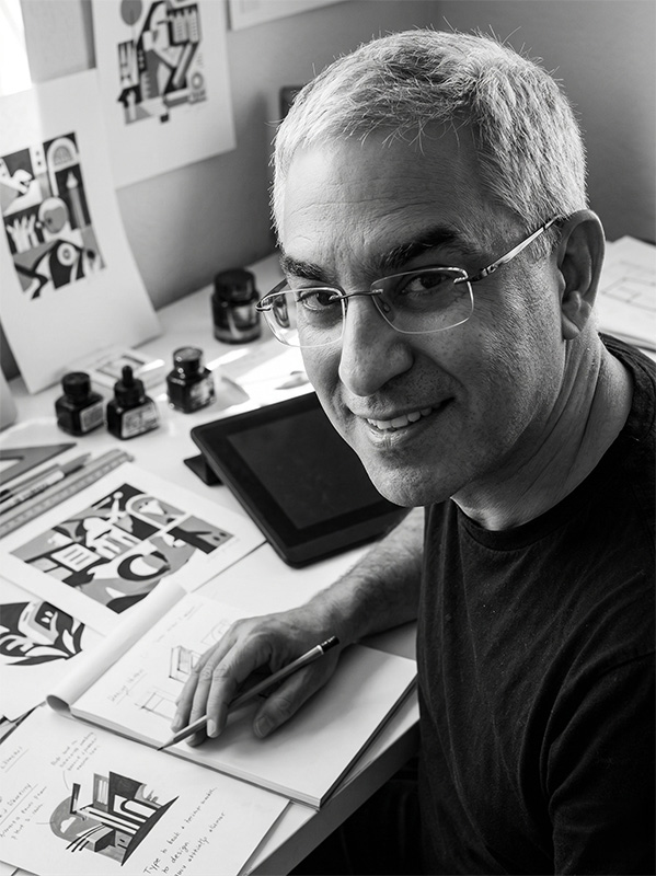 Yuval Abraham, graphic designer, sketching at his desk surrounded by illustration work, ink bottles and design materials